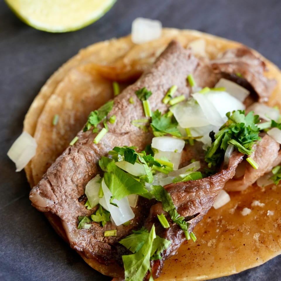 A close-up of a carne asada taco with onions and cilantro, next to a lime wedge.