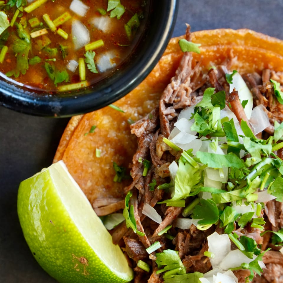 Señor Jalalpeño's birria taco with shredded beef, cilantro, onions, lime, and a side of consommé.