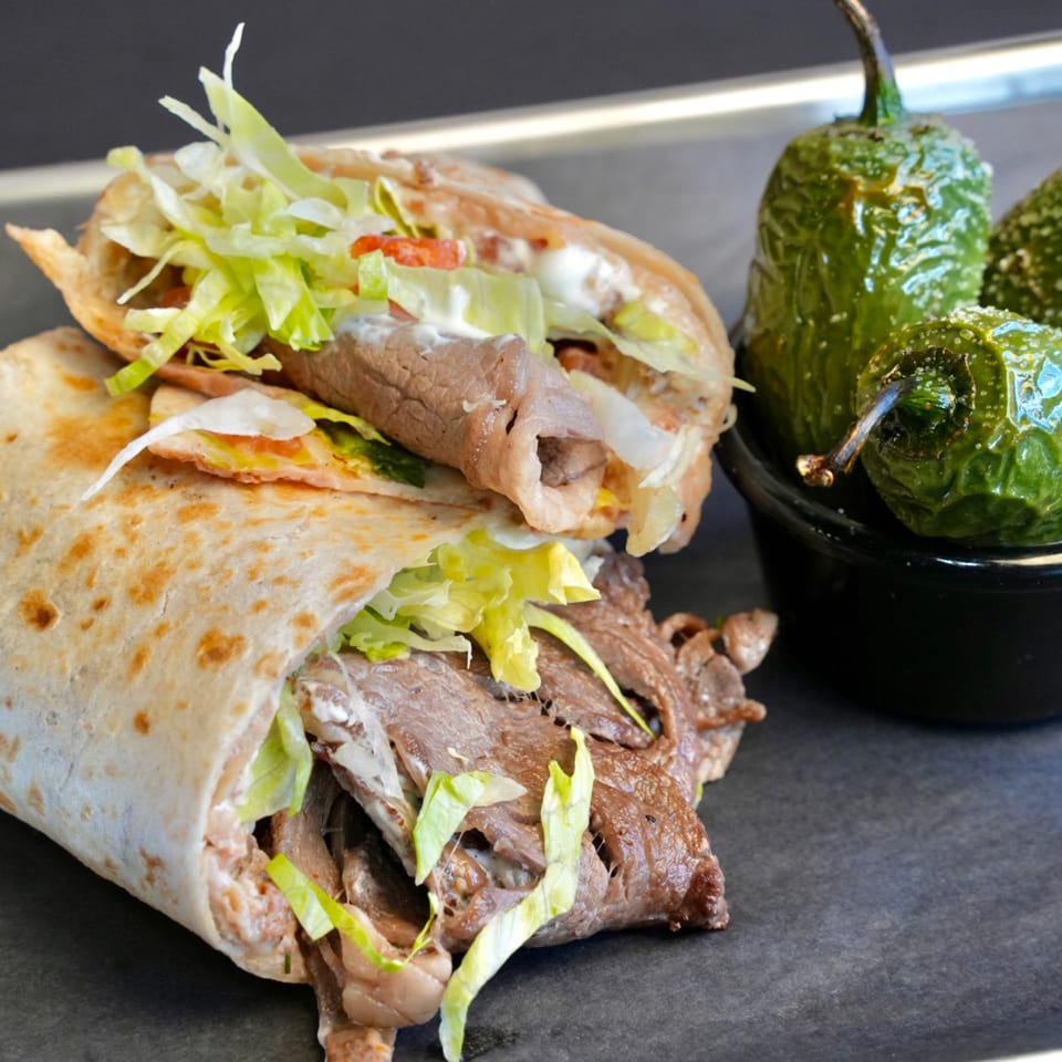 Two beef tacos with lettuce and sour cream, next to a small bowl of roasted green peppers.