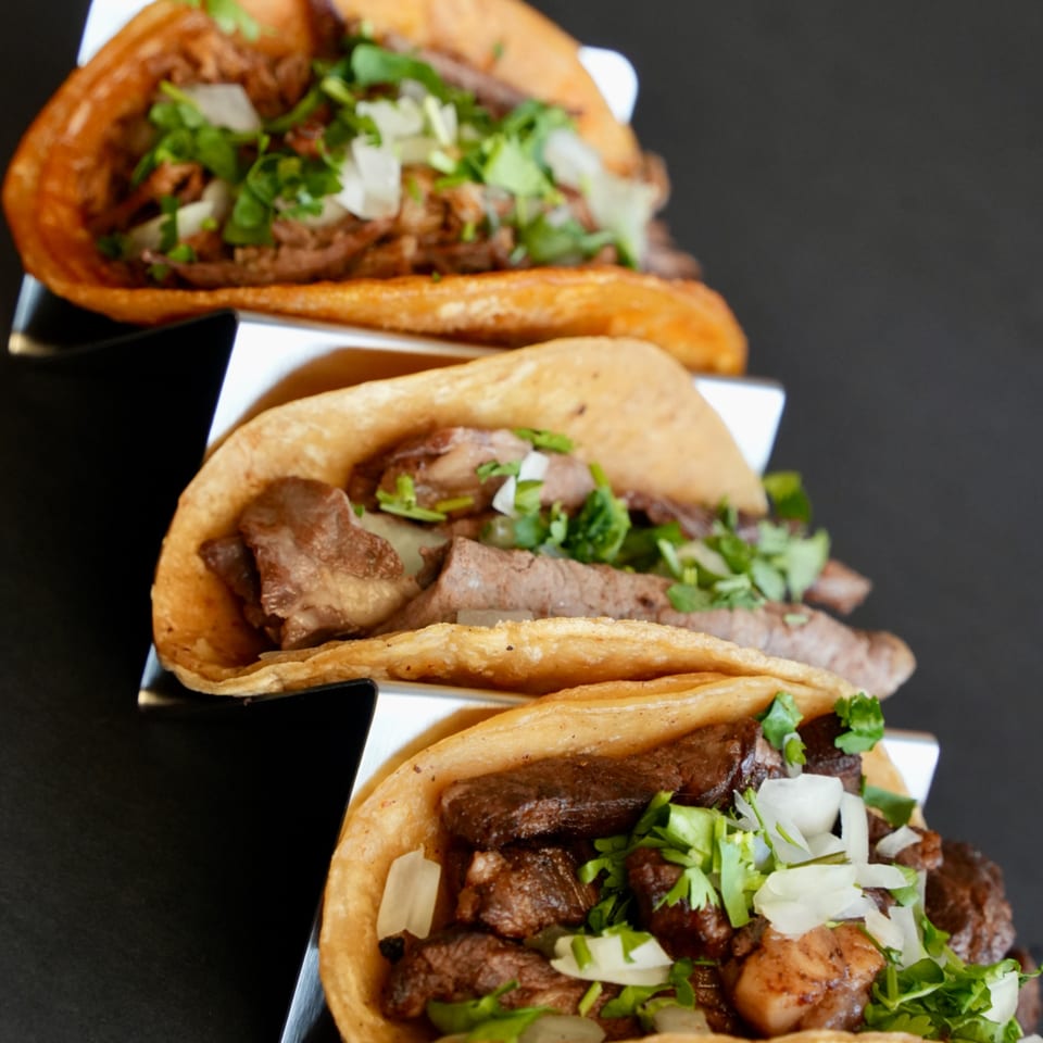 Three delicious Señor Jalapeño tacos with meat, cilantro, and onions in a metal holder.