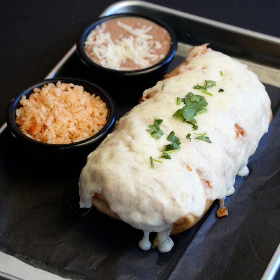 A large, cheese-covered burrito with cilantro, served with Mexican rice and refried beans.